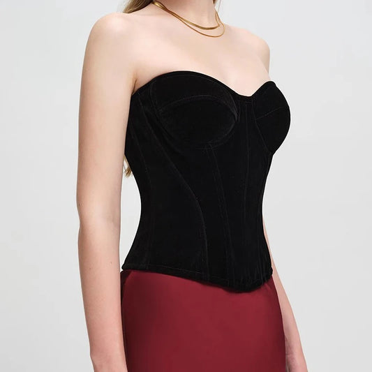 A model wearing a black velvet strapless corset top paired with a dark red skirt, shown from the shoulders to the hips against a light gray studio background.