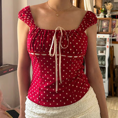 Person wearing a red polka dot top with a white skirt in an indoor setting