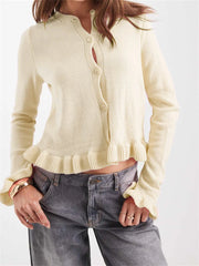 Person wearing a light yellow cardigan over a white shirt with gray pants on a plain background
