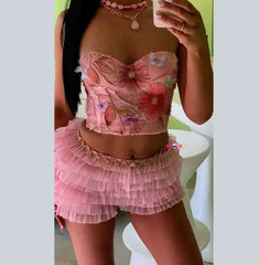 Woman wearing a pink floral top and skirt set, holding a drink.