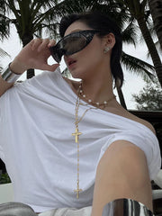 Woman wearing sunglasses and a white top with a necklace, palm trees in the background