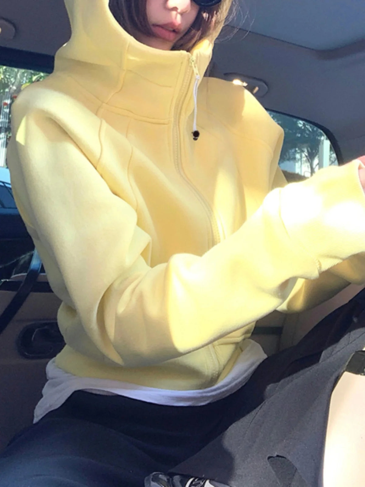 Person wearing a yellow hoodie sitting inside a vehicle.