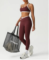 Person wearing a burgundy sports bra and leggings holding a black shopping bag.