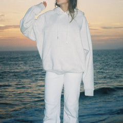 Person wearing a white outfit standing by the ocean at sunset