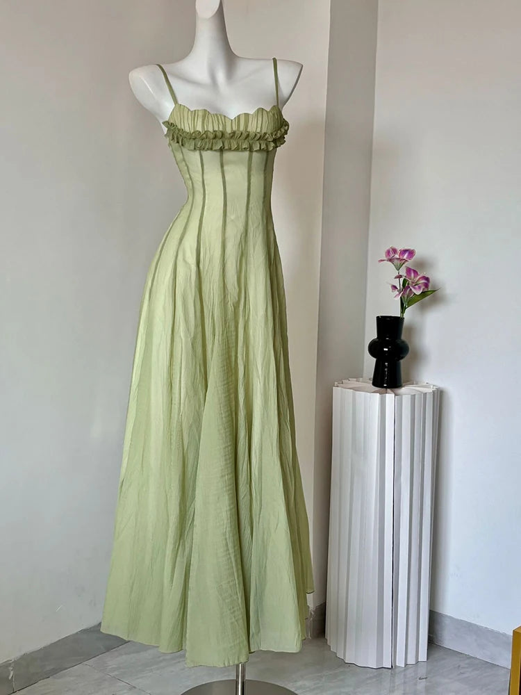 Green dress on a mannequin against a plain wall with a vase of flowers on a pedestal.