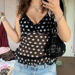 Person wearing a black polka dot top and blue jeans, holding a black bag.