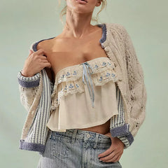 Woman wearing a beige cardigan over a floral top and jeans on a light green background