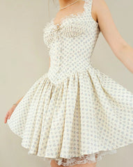 A sleeveless cream-colored swing dress with a small blue floral pattern, featuring a ruffled sweetheart neckline, lace trim, and a flared skirt, shown on a model against a neutral beige background.