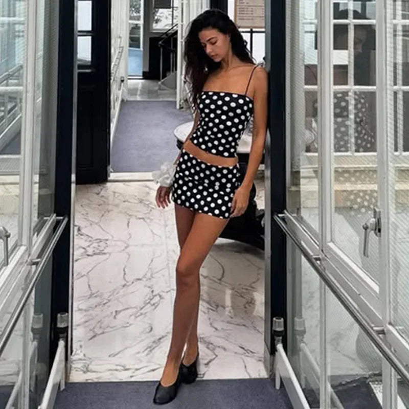 Woman in a black and white polka dot dress standing in a modern interior setting.