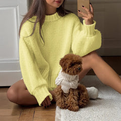 Person wearing a bright yellow sweater sitting on the floor with a small brown dog wearing a white sweater.