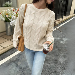 Person wearing a cream sweater and light blue jeans, holding a drink on a street.