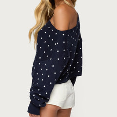Navy blue sweater with white polka dots worn by a person on a light gray background