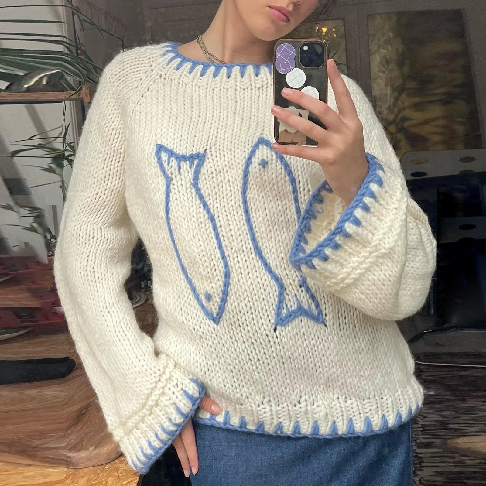 Person wearing a white sweater with blue fish designs, taking a mirror selfie.